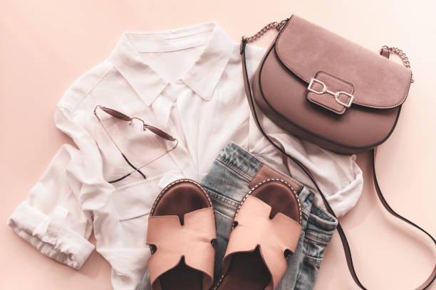 Feminine summer fashion flat lay with blouse, handbag, sunglasses, shorts and slippers on beige background. Top view.